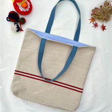 Load image into Gallery viewer, Tote bag. Heavyweight natural woven canvas with two horizontal red stripes. Lined with an ex-designer striped cotton shirting fabric.