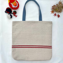Load image into Gallery viewer, Tote bag. Heavyweight natural woven canvas with two horizontal red stripes. Lined with an ex-designer striped cotton shirting fabric.