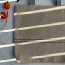 Load image into Gallery viewer, Tote bag. Heavyweight natural woven canvas with two horizontal sand-coloured stripes. Lined with a striped cotton shirting fabric.