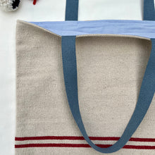 Load image into Gallery viewer, Tote bag. Heavyweight natural woven canvas with two horizontal red stripes. Lined with an ex-designer striped cotton shirting fabric.

