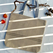 Load image into Gallery viewer, Tote bag. Heavyweight natural woven canvas with two horizontal sand-coloured stripes. Lined with a striped cotton shirting fabric.
