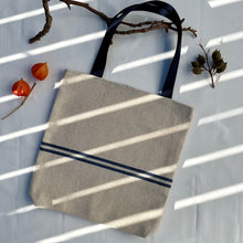 Load image into Gallery viewer, Tote bag. Heavyweight natural woven canvas with two horizontal blue stripes. Lined with a striped cotton shirting fabric.
