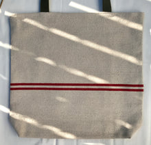 Load image into Gallery viewer, Tote bag. Heavyweight natural woven canvas with two horizontal red stripes. Lined with a beautiful striped cotton shirting fabric.
