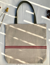 Load image into Gallery viewer, Tote bag. Heavyweight natural woven canvas with two horizontal red stripes. Lined with a beautiful striped cotton shirting fabric.

