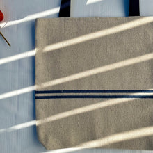 Load image into Gallery viewer, Tote bag. Heavyweight natural woven canvas with two horizontal blue stripes. Lined with a striped cotton shirting fabric.
