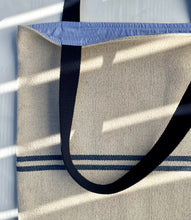 Load image into Gallery viewer, Tote bag. Heavyweight natural woven canvas with two horizontal blue stripes. Lined with a striped cotton shirting fabric.
