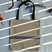Load image into Gallery viewer, Tote bag. Heavyweight natural woven canvas with two horizontal blue stripes. Lined with a striped cotton shirting fabric.
