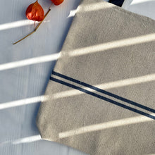 Load image into Gallery viewer, Tote bag. Heavyweight natural woven canvas with two horizontal blue stripes. Lined with a striped cotton shirting fabric.
