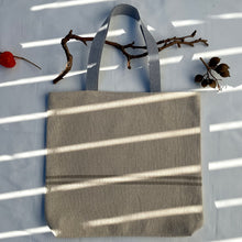 Load image into Gallery viewer, Tote bag. Heavyweight natural woven canvas with two horizontal sand-coloured stripes. Lined with a striped cotton shirting fabric.
