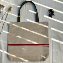 Load image into Gallery viewer, Tote bag. Heavyweight natural woven canvas with two horizontal red stripes. Lined with a beautiful striped cotton shirting fabric.
