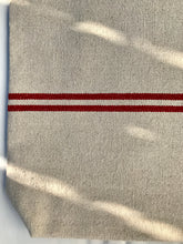 Load image into Gallery viewer, Tote bag. Heavyweight natural woven canvas with two horizontal red stripes. Lined with a beautiful striped cotton shirting fabric.
