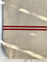 Load image into Gallery viewer, Tote bag. Heavyweight natural woven canvas with two horizontal red stripes. Lined with a beautiful striped cotton shirting fabric.
